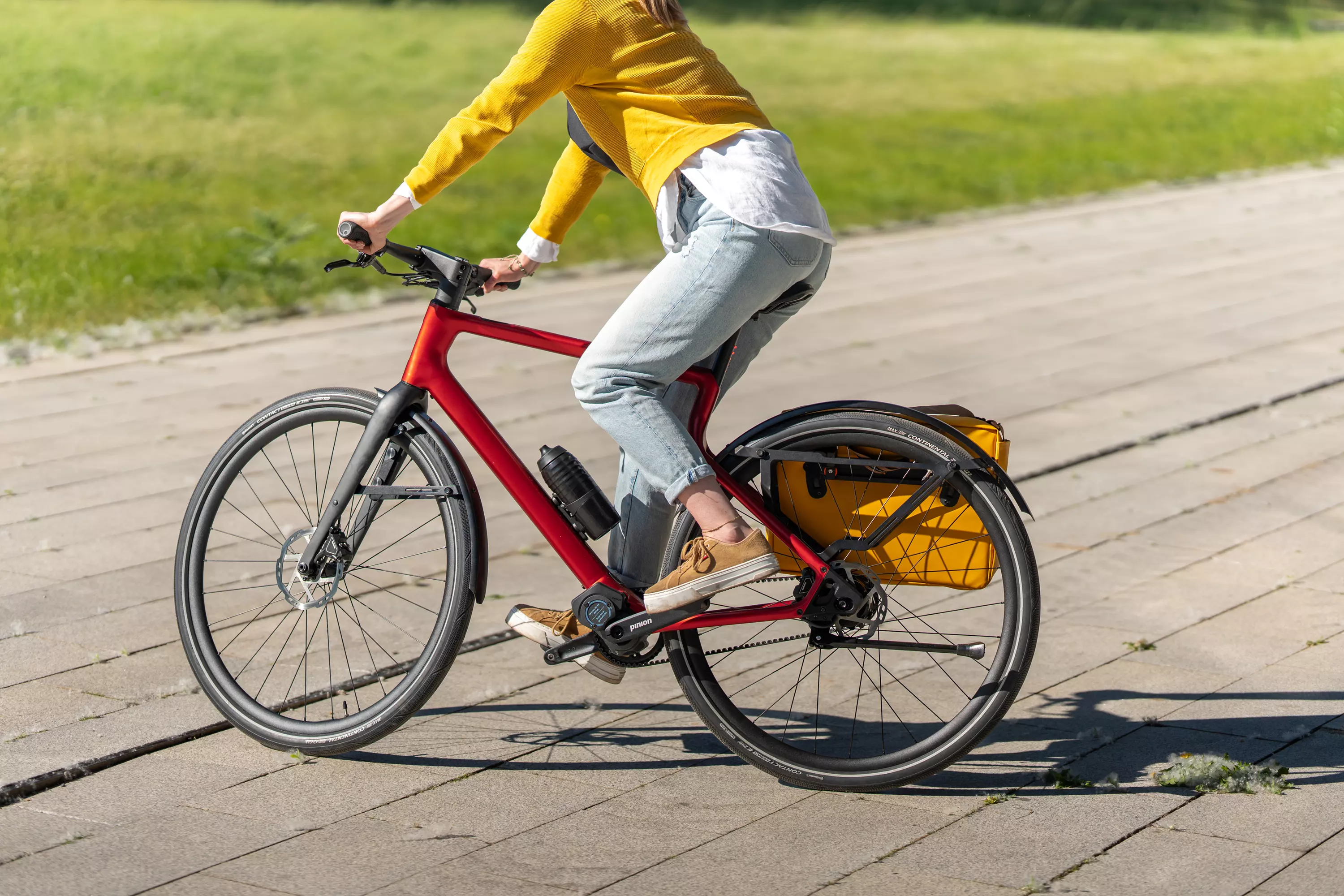 Eine junge modebewusste Frau fährt mit dem roten E-Bike Stadtfuchs inklusive Helm und Radtasche auf der Straße in der Stadt