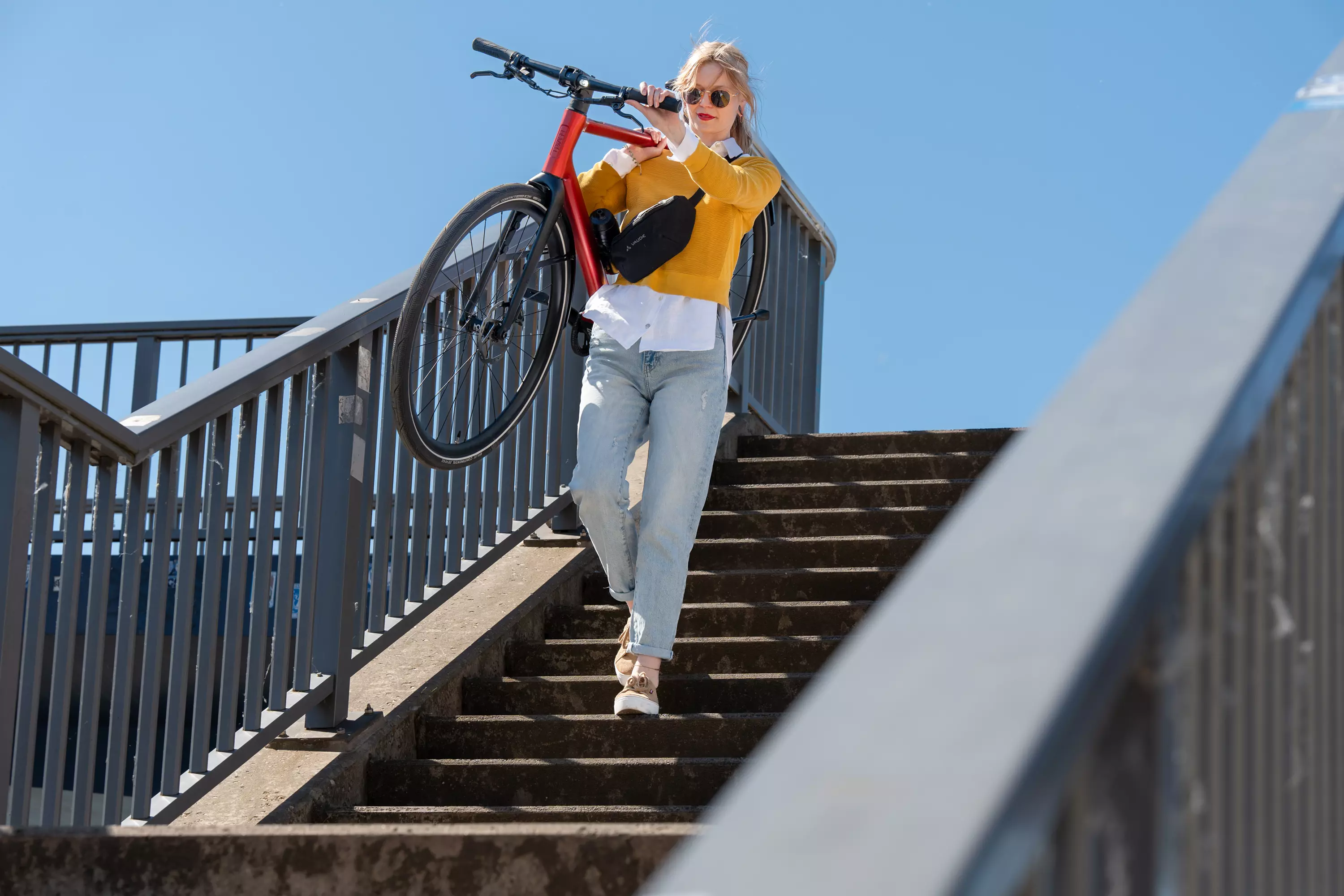 Eine junge modebewusste Frau trägt ihr Urban E-Bike Stadtfuchs eine Treppe hinunter