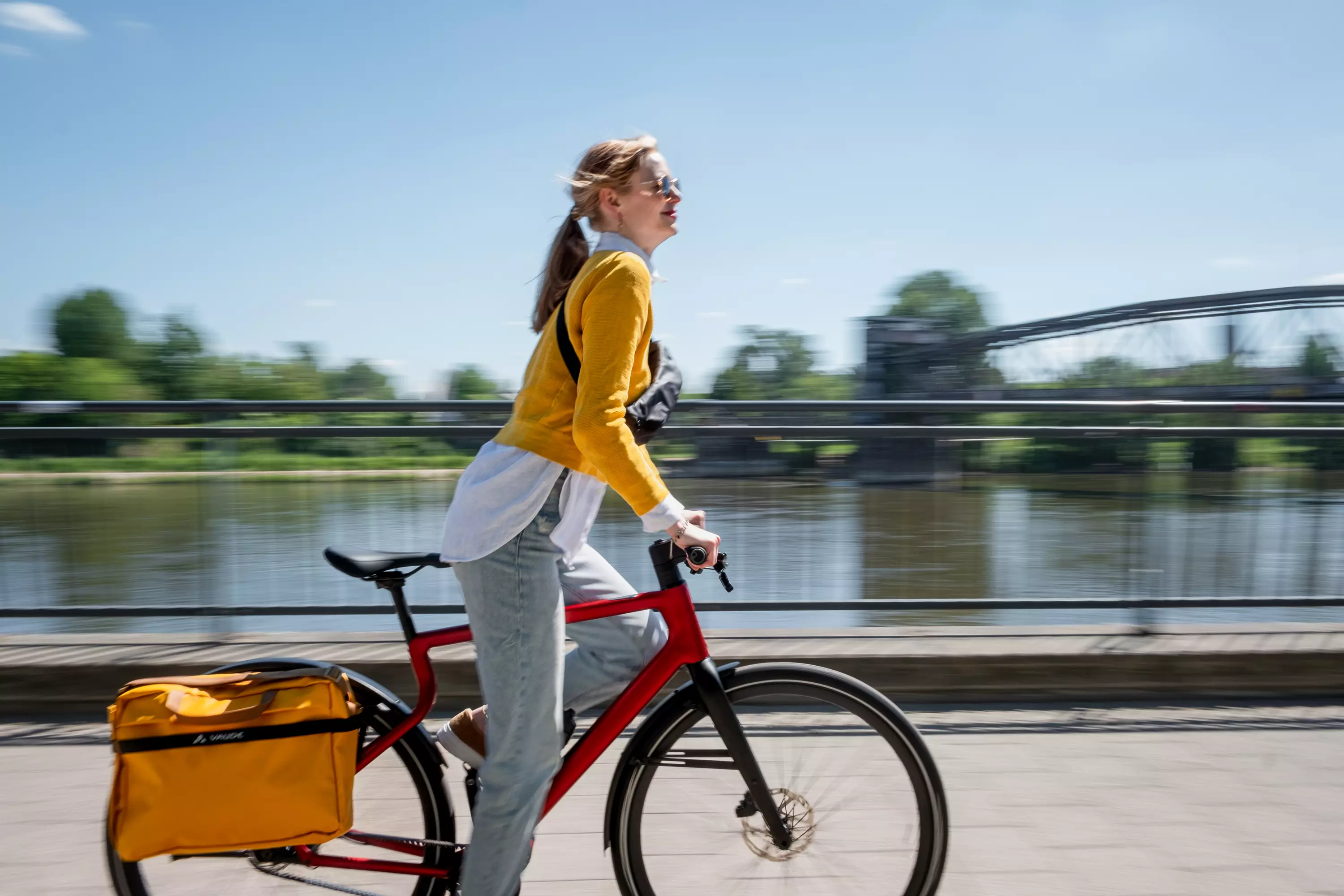 Seitenansicht der Fahrt mit dem E-Bike Stadtfuchs in Oxid Rot mit Saskia, die im Stehen in die Pedale tritt