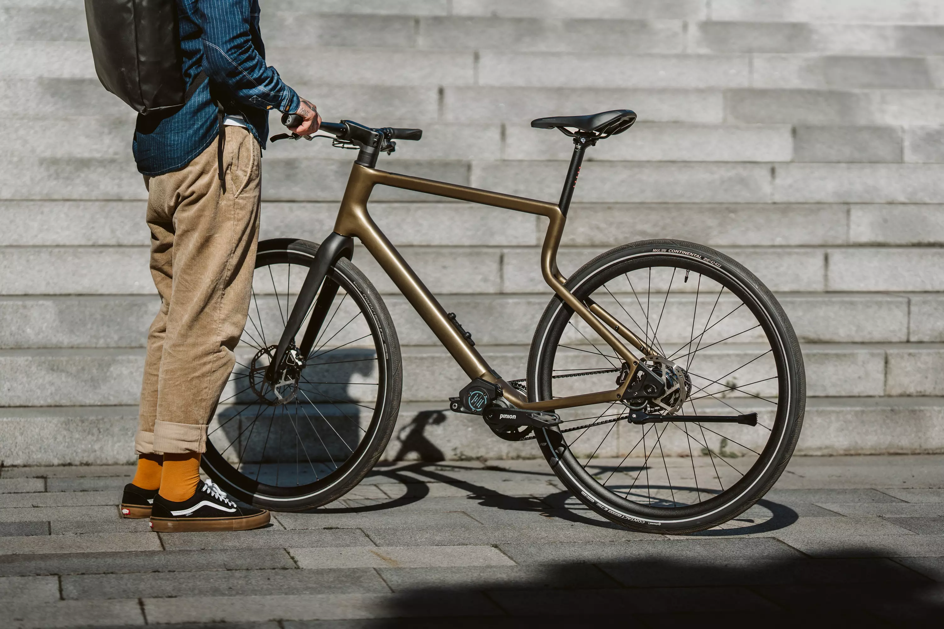 Ein junger, trendbewusster Mann steht neben seinem Urban E-Bike Stadtfuchs in Bronzebraun