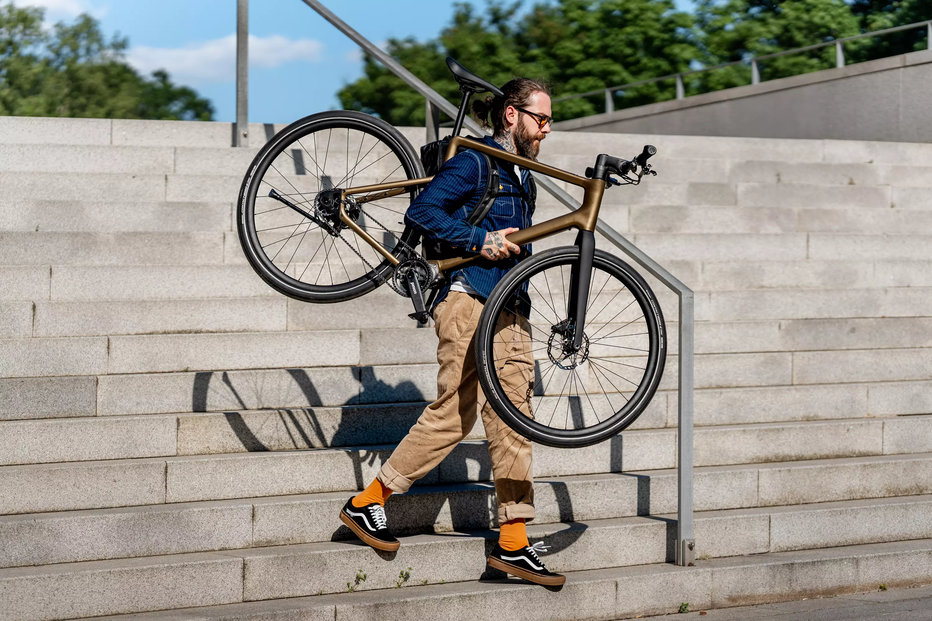 Junger, trendbewusster Mann trägt sein Stadtfuchs Urban E-Bike geschultert eine Treppe herunter