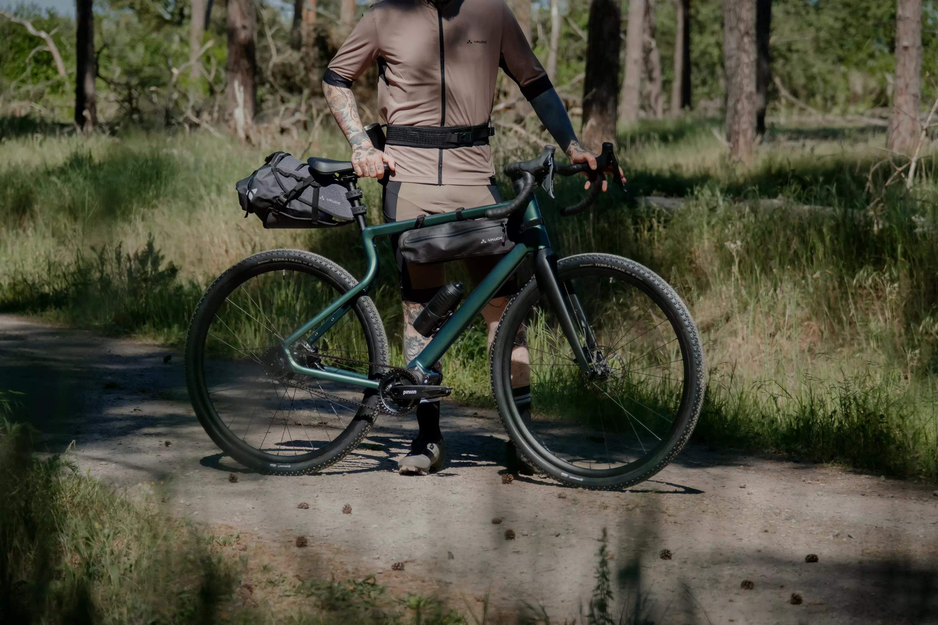 Sportlicher junger Mann steht neben dem asphaltfarbenen Gravel Bike Waldwiesel vor einem verschlossenen Garagentor