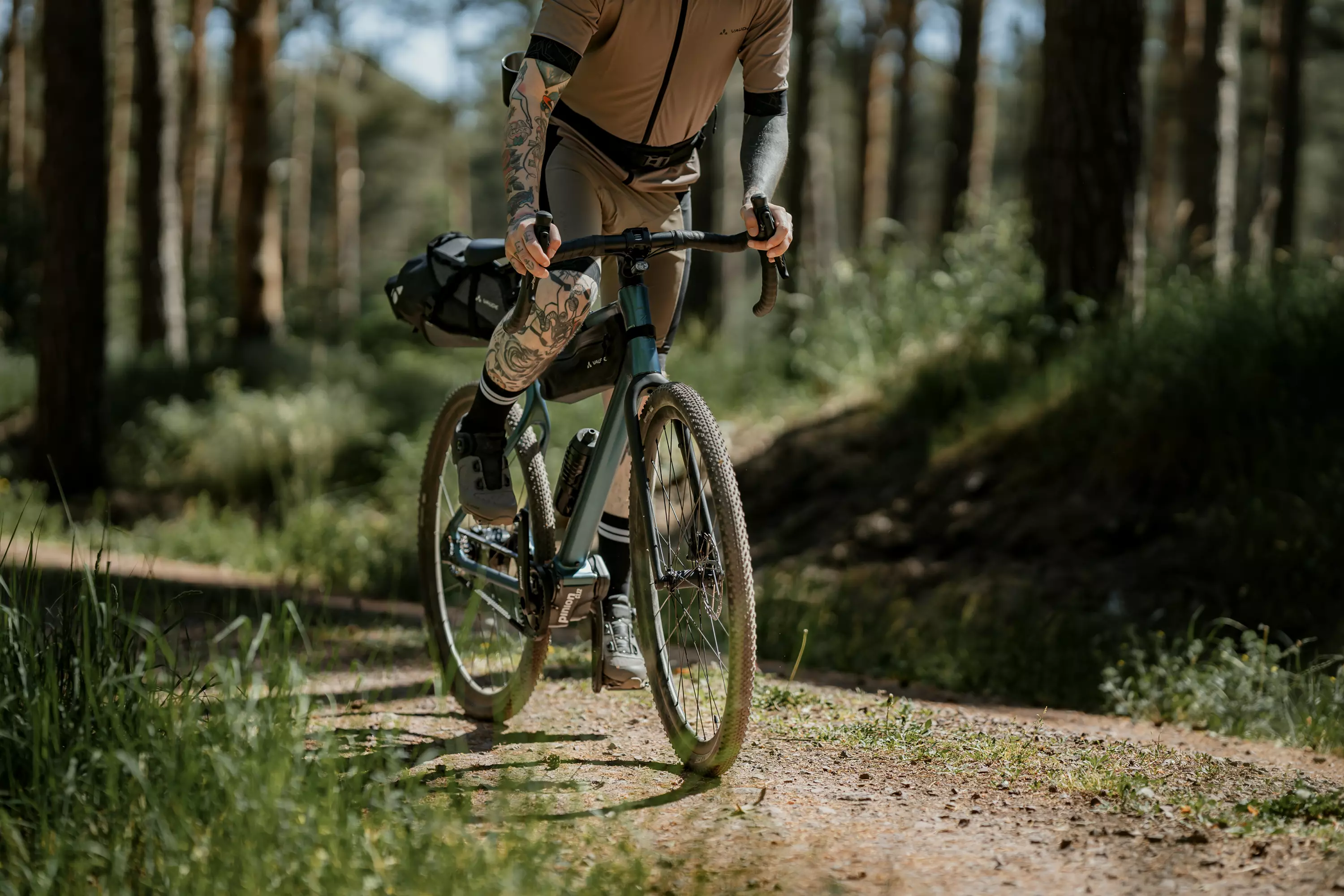 Junger Mann fährt stehend mit seinem Gravel E-Bike Waldwiesel auf einem Schotterweg durch den Wald