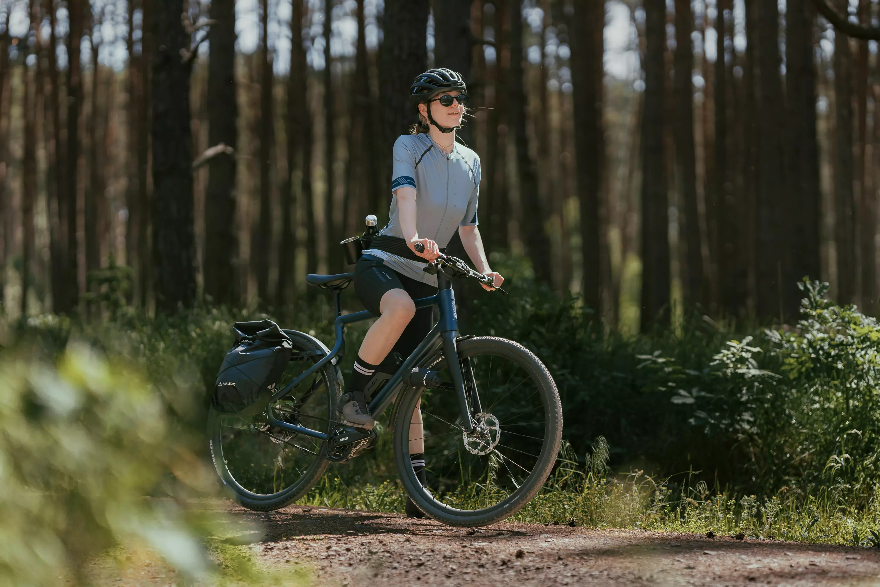 Junge Frau steht mit Gepäck mit ihrem Gravel E-Bike Waldwiesel im Wald