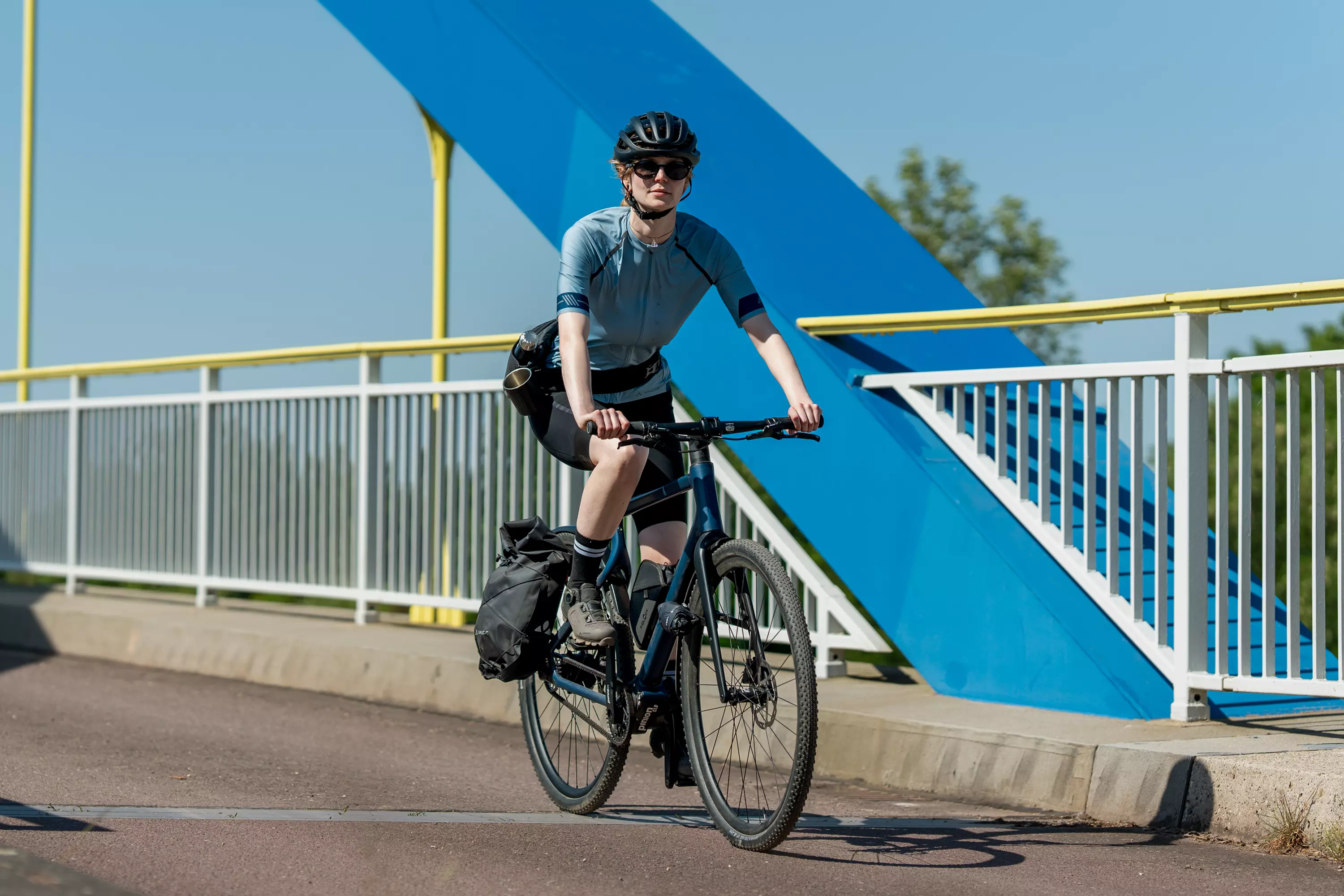 Junge Frau in sportlicher Ausstattung fährt mit ihrem Gravel E-Bike Waldwiesel über eine Brücke