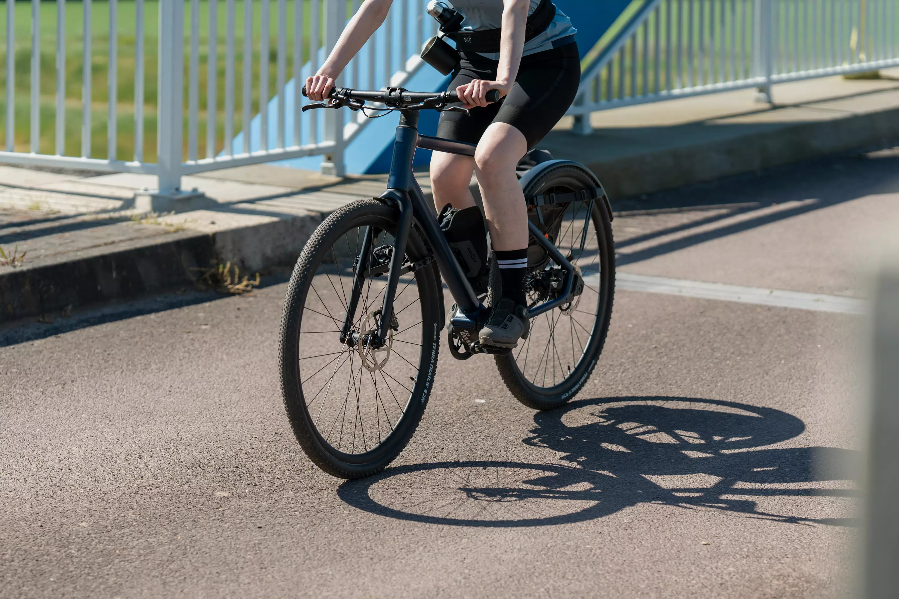 Junge Frau in sportlicher Ausstattung fährt mit ihrem Gravel E-Bike Waldwiesel über eine Brücke