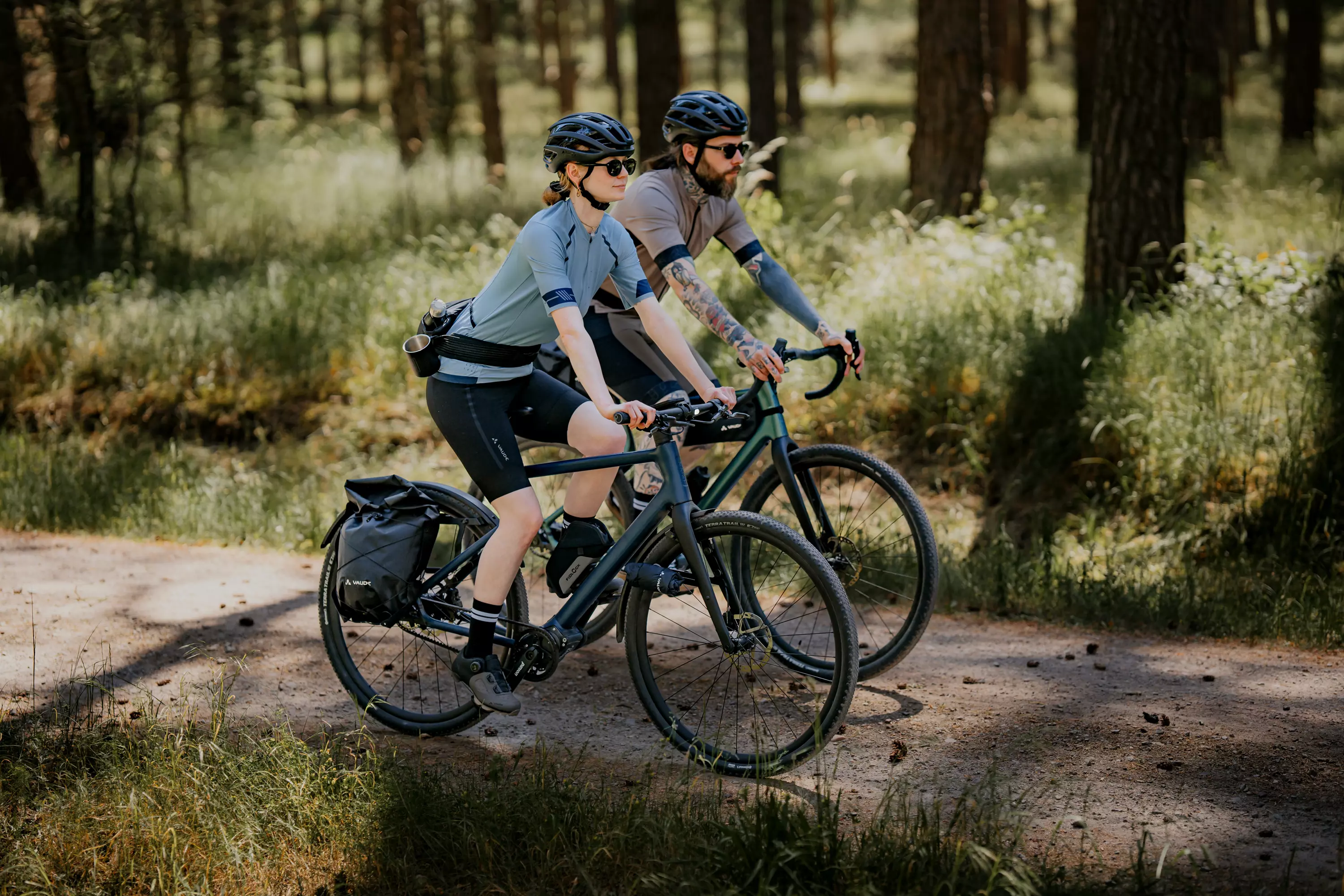 Zwei Radfahrer sausen bei sonnigem Wetter mit dem Waldwiesel Gravel Bike um eine Kurve auf dem Schotterweg