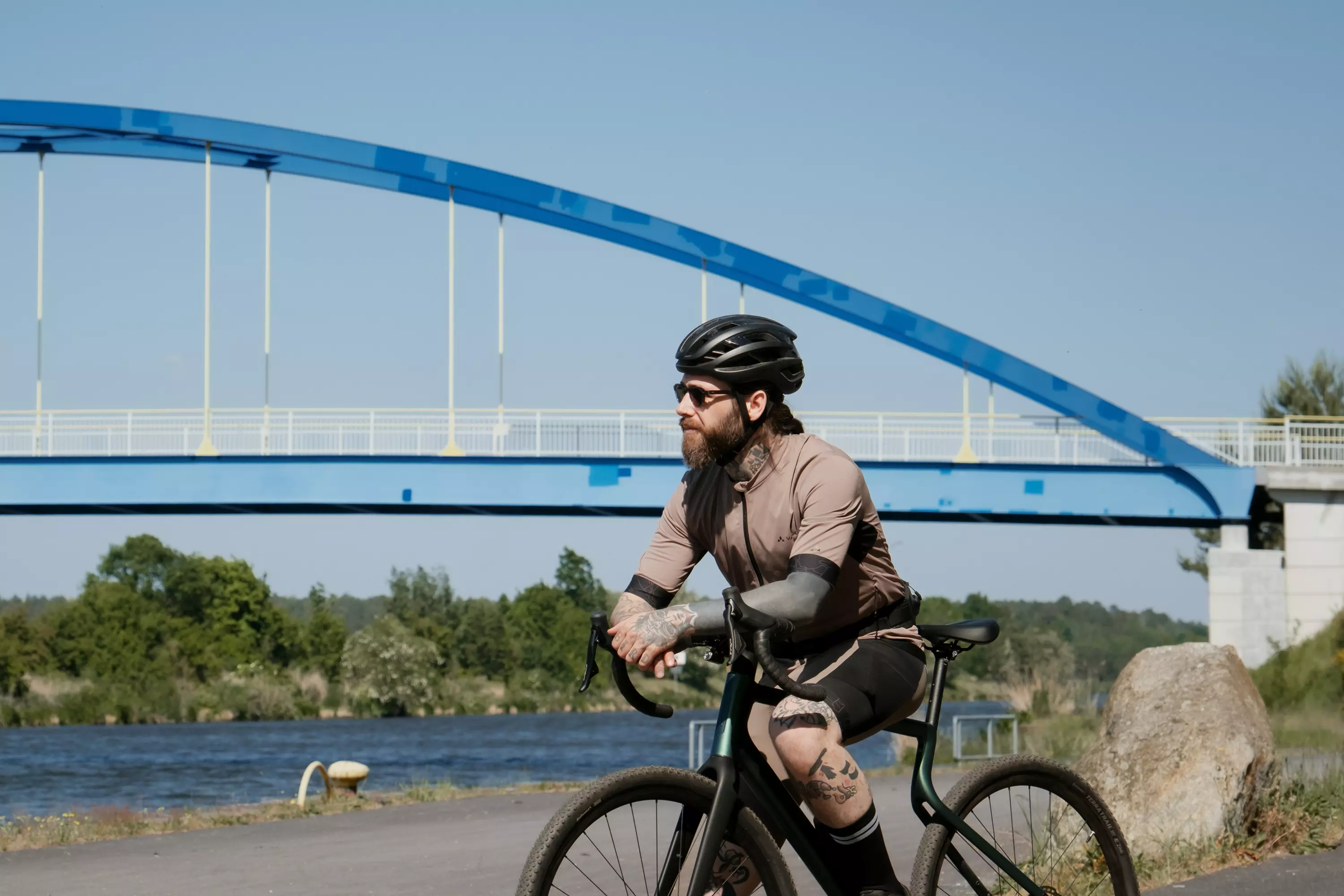 Sportlicher junger Mann pausiert nach einer Graveltour mit dem Gravel Bike Waldwiesel auf einer grünen Wiese am Wegesrand