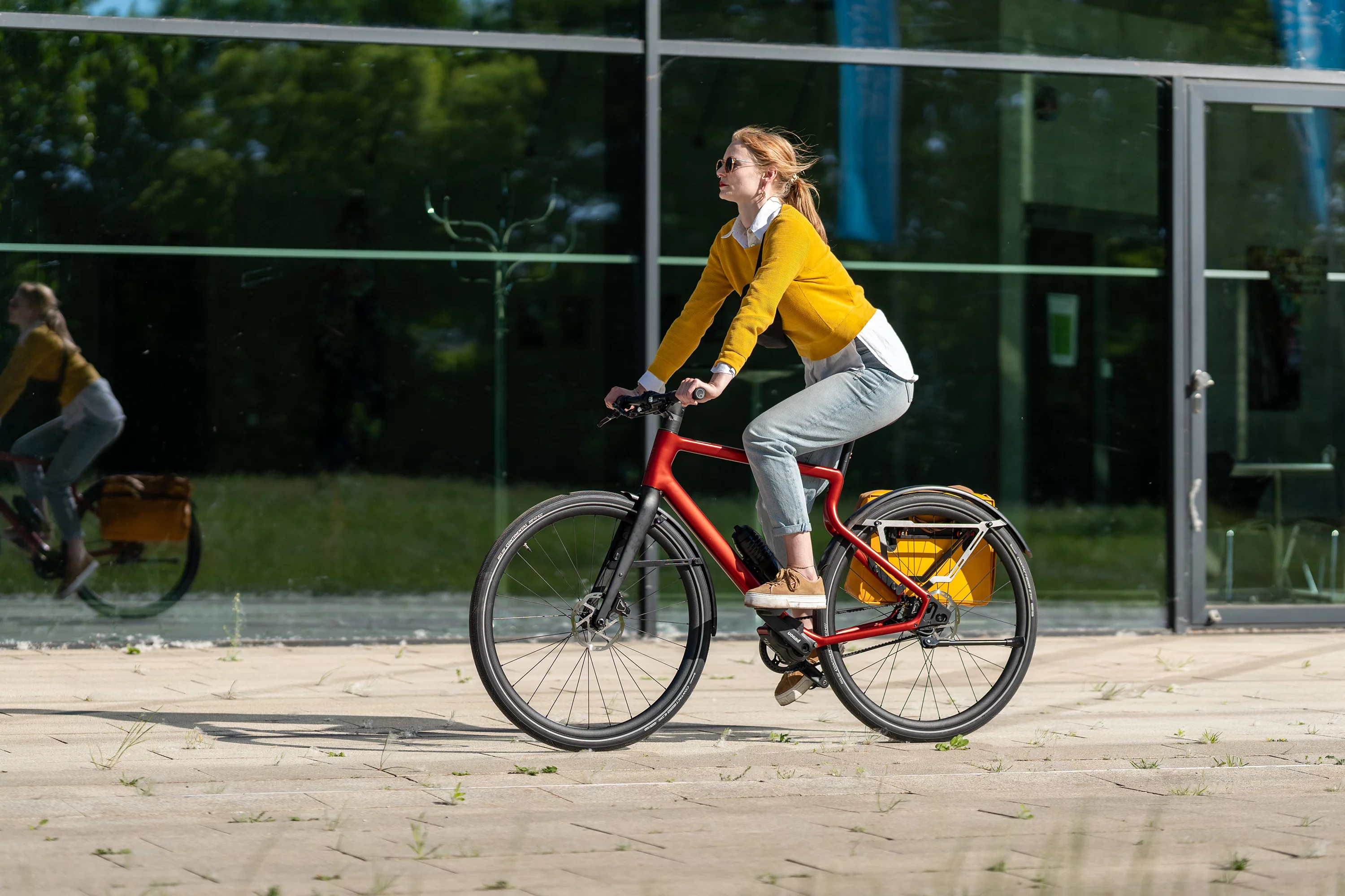 Junge hippe Frau fährt mit dem Urban E-Bike Stadtfuchs in Oxidrot durch die Stadt