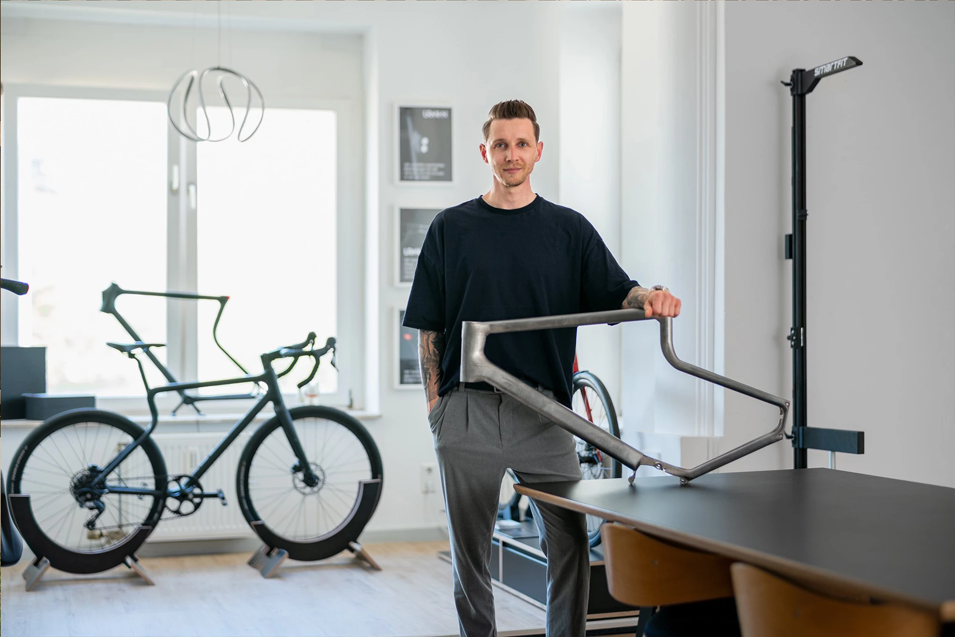 URWAHN Gründer und Geschäftsführer Sebastian Meinecke stehend im URWAHN Showroom, den Unterarm gelehnt auf einem Fairframe Stahlrahmen mit Softride 2.0