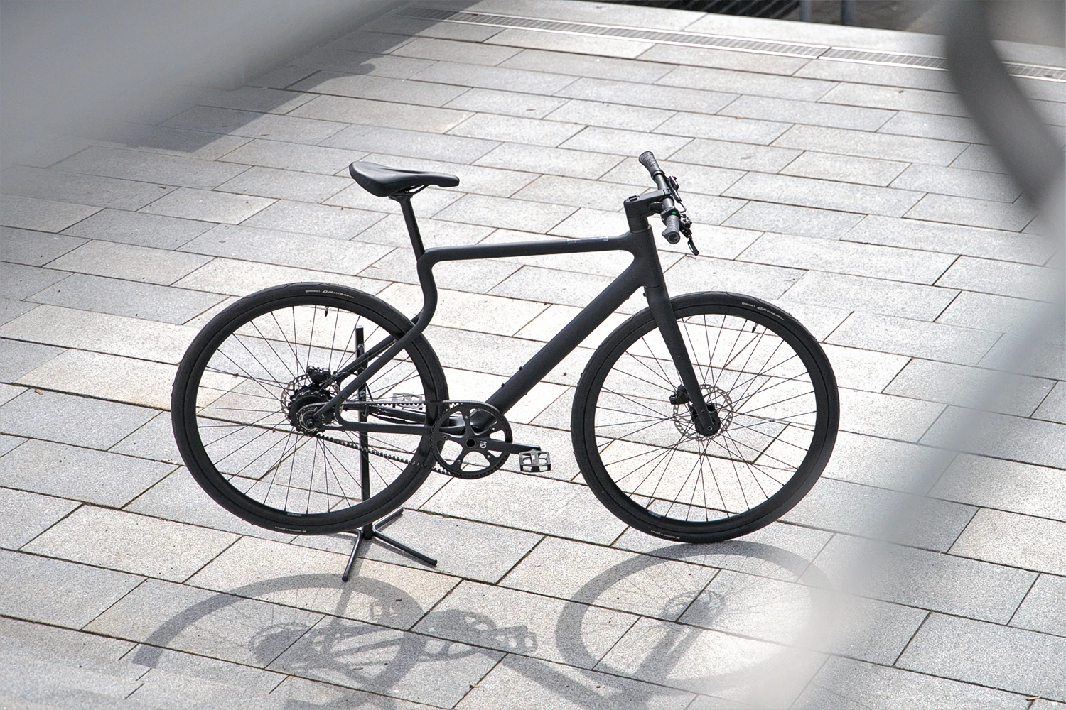 E-Bike Stadtfuchs in Asphaltschwarz steht am Fuße einer Treppe auf Betonuntergrund
